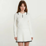 Woman wearing a white long-sleeve dress with black trim on a plain background