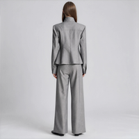 A model viewed from the back wearing a light gray two-piece suit with a structured blazer and wide-leg trousers, set against a plain light gray studio background.