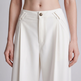 A close-up of a model wearing high-waisted, wide-leg trousers in an off-white or cream color. The trousers feature a structured waistband with a single gold-tone button, diagonal welt pockets, and a clean, minimalist design.