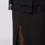 Close-up of a black dress featuring a high side slit with sheer floral lace lining, a matching black lace band at the waist, and black lace-trimmed cuffs.
