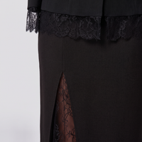 Close-up of a black dress featuring a high side slit with sheer floral lace lining, a matching black lace band at the waist, and black lace-trimmed cuffs.