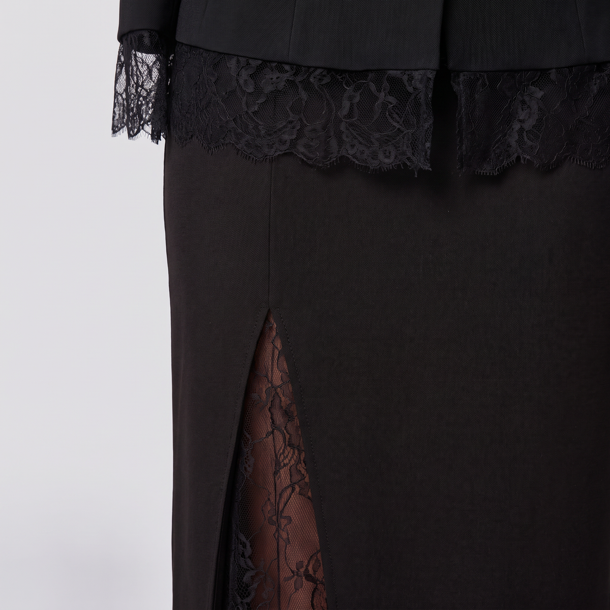 Close-up of a black dress featuring a high side slit with sheer floral lace lining, a matching black lace band at the waist, and black lace-trimmed cuffs.