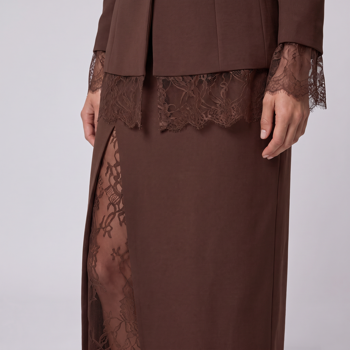 A close-up of a brown dress with a matching jacket, featuring sheer lace trim at the waist and cuffs, and a side slit showing the underlayer.