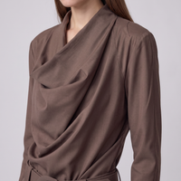 A close-up of a model wearing a brown draped wrap-style blouse with long sleeves and a matching tie belt, shown against a light gray studio background.