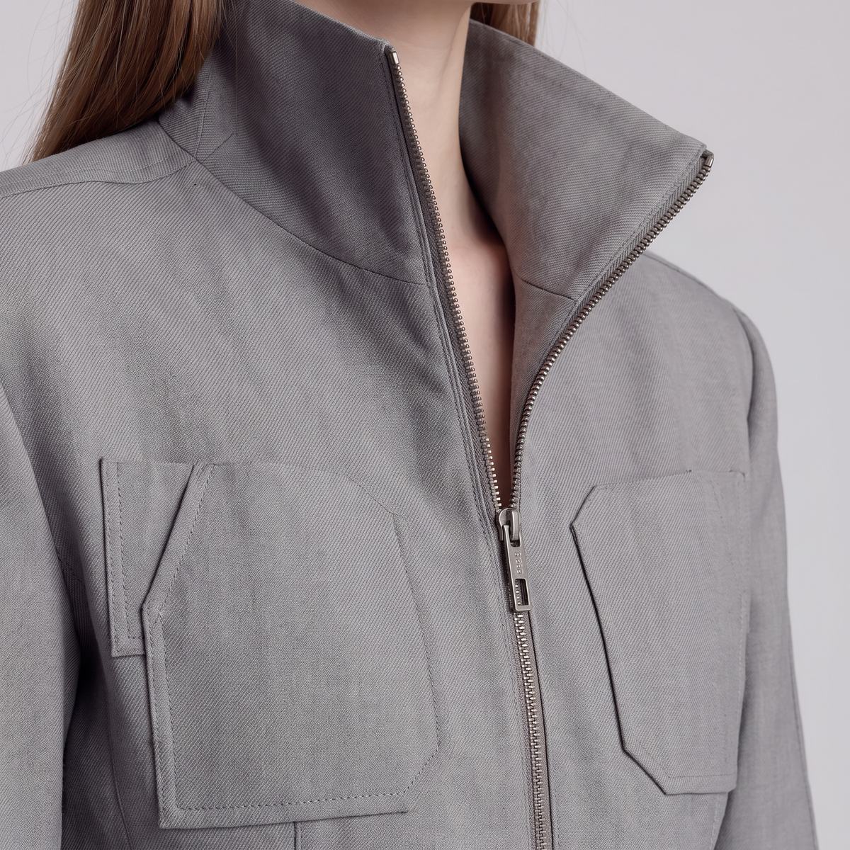 Close-up of a person wearing a light gray zip-front jacket with a high stand collar and two large front patch pockets.