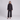 A model stands against a light gray studio background wearing a black long-sleeve belted jacket with a high mock neck and matching wide-leg trousers.