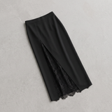 A black midi skirt with a front slit revealing a black lace underlayer, laid flat on a light gray textured background.