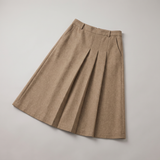 A beige pleated A-line skirt with side pockets, laid flat on a light gray background.