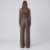 A woman viewed from behind wearing a matching brown long-sleeve top and wide-leg trousers set with a matching belt, against a plain light gray studio background.