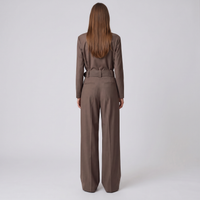 A woman viewed from behind wearing a matching brown long-sleeve top and wide-leg trousers set with a matching belt, against a plain light gray studio background.