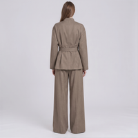 A model viewed from the back wearing a taupe-brown belted blazer and matching wide-leg trousers against a light gray studio background.