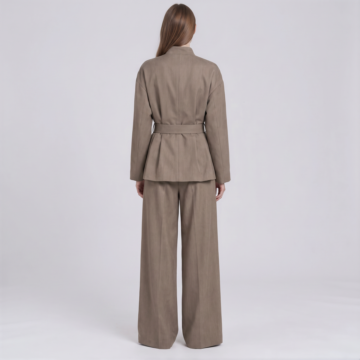 A model viewed from the back wearing a taupe-brown belted blazer and matching wide-leg trousers against a light gray studio background.