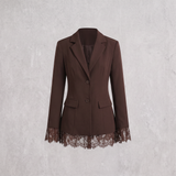 A dark brown blazer-style jacket with notched lapels, two front buttons, flap pockets, and a lace hem detail, shown against a light gray textured background.