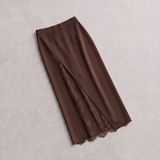 A brown midi skirt with a front slit revealing a matching lace lining, laid flat on a textured light gray background.