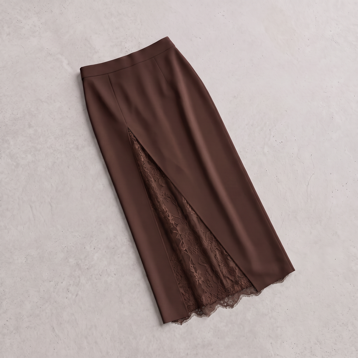 A brown midi skirt with a front slit revealing a matching lace lining, laid flat on a textured light gray background.