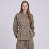 A woman modeling a taupe-brown belted jacket with a matching pair of trousers against a light gray studio background.