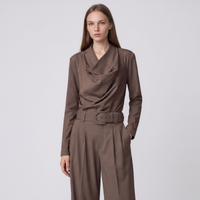 A woman modeling a brown draped long-sleeve top and matching wide-leg trousers with a matching belt, set against a plain light gray studio background.