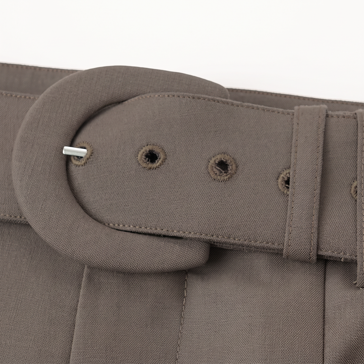 Close-up of a taupe-brown fabric belt with a large oval buckle and metal eyelets, shown against a plain white background.