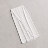 A white midi skirt with a front slit revealing a white lace lining, laid flat on a textured light gray background.
