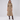 A woman modeling a beige double-breasted midi coat with a matching pleated skirt, paired with dark brown knee-high boots, against a light gray studio background.