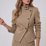 A woman wearing a beige textured wrap-style jacket with a high mock neck and three brown buttons, paired with a matching skirt, against a light gray studio background.